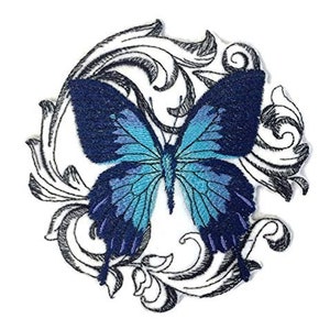 Könnte beinhalten: Ein gestickter Bügel-Patch mit einem blauen Schmetterling mit filigranen Flügeln vor einem weißen Hintergrund mit einem schwarzen floralen Design.