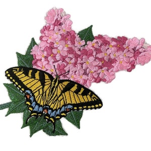 May include: A yellow and black butterfly with blue accents is perched on a cluster of pink lilac flowers. The butterfly and flowers are embroidered on a green fabric.