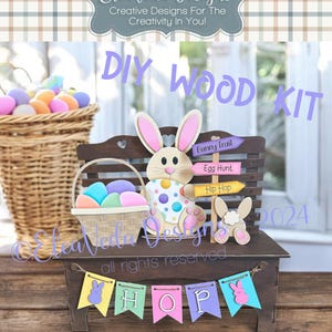 May include: DIY wood craft kit featuring a bunny rabbit, a bench, and a basket of Easter eggs. The kit includes signs that say "Bunny Trail", "Egg Hunt", and "Hip Hop". The bench has a banner that says "HOP" with bunny rabbit cutouts. The kit is designed for Easter.