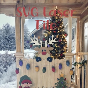 May include: A wooden Christmas-themed display featuring a reindeer, elf, and Christmas tree. The display includes colorful string lights and the text "SVG Laser File". The background shows a snowy winter scene.