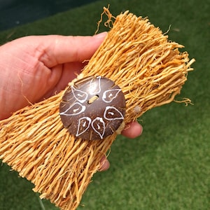May include: A bundle of thin, light brown, dried plant fibres, possibly roots, held together with a dark brown, round button. The button is decorated with white leaf-shaped designs. The background is green.