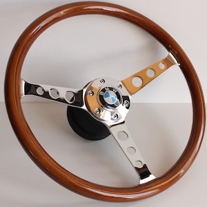 May include: A brown wood steering wheel with a chrome centre and spokes. The centre has a BMW logo.