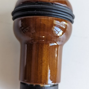 May include: A brown wooden gear shift knob with a black rubber grip. The knob has a glossy finish.