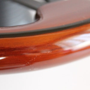Puede incluir: Primer plano de un volante de madera marr&oacute;n oscuro con un ribete negro. La madera tiene un acabado brillante.