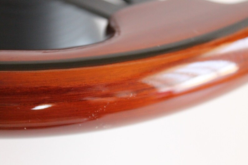 Puede incluir: Primer plano de un volante de madera marr&oacute;n oscuro con un ribete negro. La madera tiene un acabado brillante.