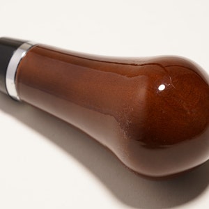 Könnte beinhalten: Ein brauner, hölzerner Schaltknauf mit schwarzem und silbernem Oberteil.