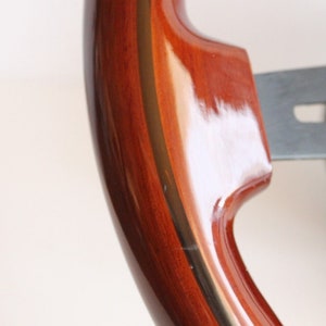 Puede incluir: Primer plano de un volante de madera con un acabado marr&oacute;n oscuro y una fina franja dorada alrededor del borde.