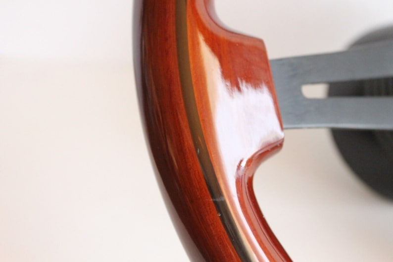 Puede incluir: Primer plano de un volante de madera con un acabado marr&oacute;n oscuro y una fina franja dorada alrededor del borde.