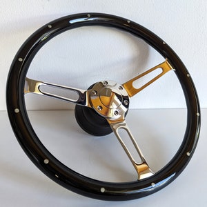 Peut inclure: Un volant de voiture classique en bois noir brillant, avec des rayons et un centre chromés. Le volant à trois branches est orné de petits rivets argentés. Le diamètre est d'environ 38 cm.