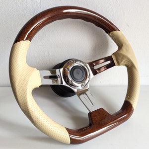 May include: A brown wood steering wheel with a beige leather grip and chrome accents. The steering wheel has a perforated leather design and a chrome center cap.