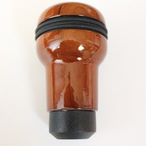 May include: A brown wooden gear shift knob with a black rubber grip. The knob has a glossy finish.