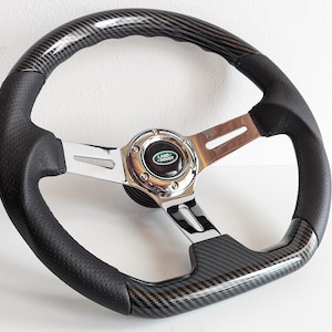Può includere: Volante in pelle nera con finitura in fibra di carbonio e mozzo centrale cromato. Il mozzo centrale presenta il logo Land Rover.