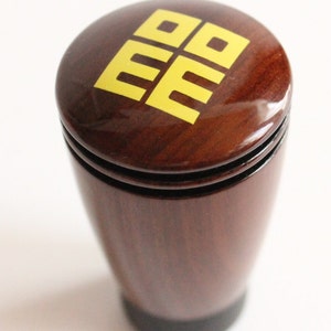 Könnte beinhalten: Ein hölzerner Schaltknauf mit einem gelben Doppel-Glückssymbol auf der Oberseite.