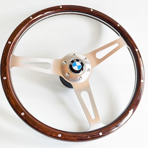 May include: A brown wood steering wheel with a silver rim and a three-spoke design. The center of the steering wheel has a silver BMW logo.