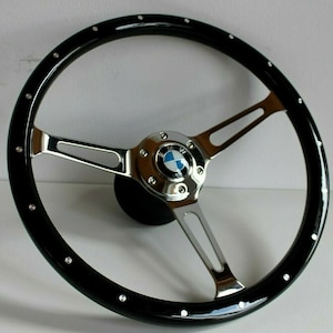 May include: A black wood steering wheel with a chrome centre and spokes. The centre has a blue and white BMW logo.