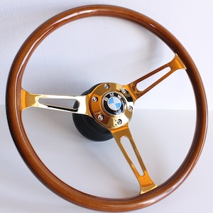 May include: A gold-plated steering wheel with a wood rim and a BMW logo in the center. The steering wheel has three spokes.