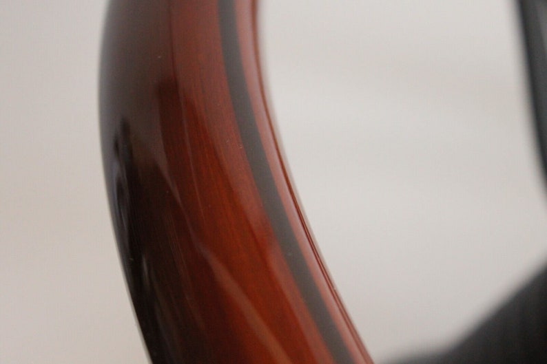 Puede incluir: Primer plano de un volante de madera con un borde marr&oacute;n oscuro y un centro marr&oacute;n rojizo. La veta de la madera es visible en el centro del volante.