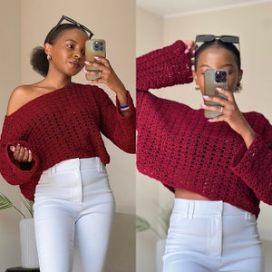 Puede incluir: Un suéter de crochet color granate con un corte holgado y mangas largas. El suéter tiene un diseño abierto y de encaje y está recortado a la cintura. La modelo lleva el suéter con pantalones blancos.