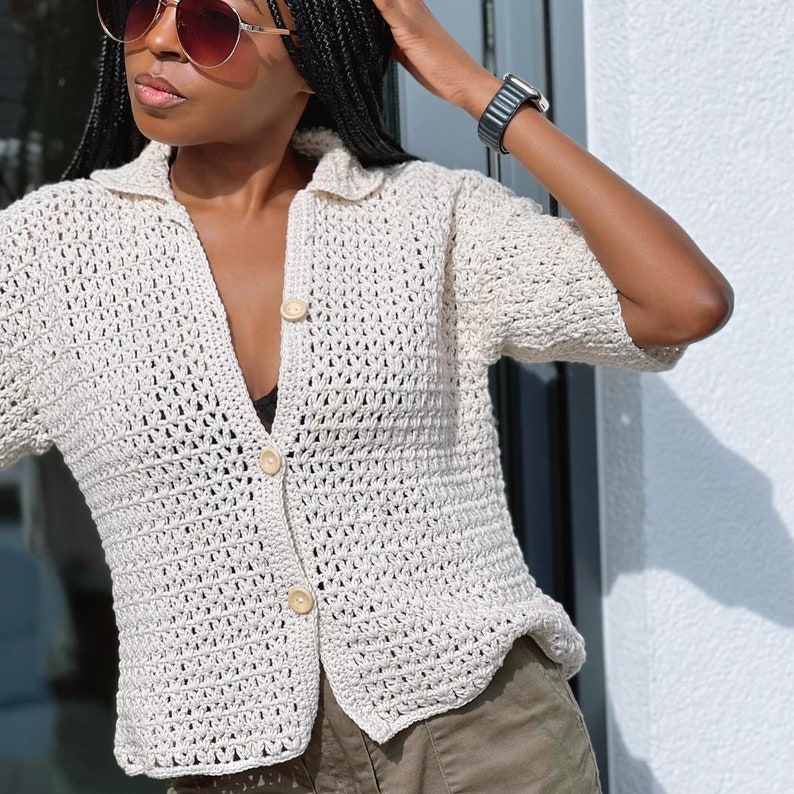 May include: A white crocheted button-up shirt with short sleeves. The shirt has a relaxed fit and is made with a lightweight yarn.