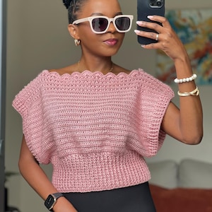 Peut inclure: Haut rose en crochet avec encolure festonnée et manches courtes. Le haut est associé à un legging noir. La personne porte des lunettes de soleil à monture blanche et tient un smartphone noir. Accessoires : boucles d'oreilles dorées et bracelet.