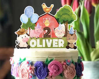 Puede incluir: Un pastel blanco con flores de glaseado de color rosa, morado y blanco. El pastel está decorado con una decoración de temática de granja con un granero rojo, una vaca, un cerdo, una oveja, un caballo, un pollo y globos. La decoración también incluye el nombre "OLIVER" y el número "2".