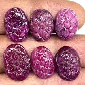 Puede incluir: Seis piedras preciosas ovaladas de color magenta intenso, cada una con un patrón floral tallado en la superficie. Las piedras están dispuestas en dos filas de tres, mostrando un acabado pulido con inclusiones naturales visibles.