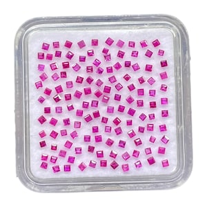 Puede incluir: Una colección de pequeñas piedras preciosas de color rosa vibrante, cortadas en forma cuadrada y dispuestas en una cuadrícula sobre una base de espuma blanca dentro de una caja de presentación cuadrada de plástico transparente.