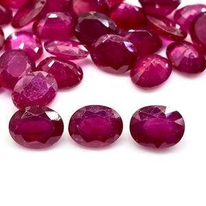 Peut inclure: Collection de rubis de taille ovale, d'un rouge profond. Les pierres précieuses sont dispersées sur une surface blanche, certaines étant nettes, soulignant leurs facettes et leur éclat. Idéal pour la création de bijoux.