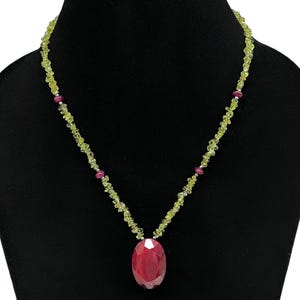 Puede incluir: Un collar que presenta una hebra de pequeñas cuentas irregulares de peridoto verde claro, acentuadas con cuatro cuentas redondas de rubí rosa intenso. Un gran colgante de rubí rosa intenso, ovalado y facetado, cuelga del centro del collar.