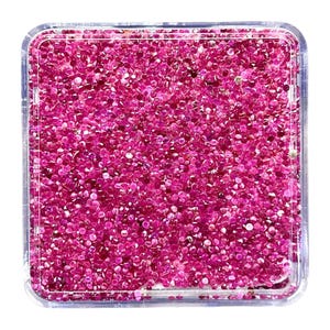 Pode incluir: Um recipiente quadrado de plástico transparente preenchido com uma grande quantidade de pequenas pedras preciosas facetadas de cor rosa vibrante. As pedras estão densamente agrupadas, exibindo vários tons de magenta e fúcsia com superfícies reflexivas.