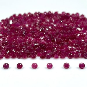 May include: A large collection of small, round, faceted deep red rubies arranged in a dense pile, with six individual rubies lined up in a horizontal row at the bottom. Each gemstone features a brilliant cut with multiple reflective surfaces.