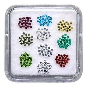 May include: A clear plastic container holding nine clusters of small, round gemstones in various colors. Colors include deep red, light blue, yellow, green, silver, and dark red. The gemstones are set against a white background.
