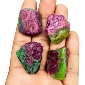 May include: Four rough, uncut gemstone specimens featuring a distinct color combination of deep magenta-pink and vibrant lime-green. Each stone displays a raw, crystalline texture with irregular, jagged edges and natural mineral inclusions.