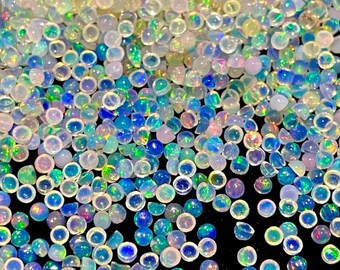 Op de afbeelding: Een verzameling kleine, ronde, doorschijnende cabochons met een iriserende afwerking. Elk stuk heeft een melkwitte basis met levendige flitsen van blauw, groen en roze licht, wat een glinsterend, veelkleurig effect op het oppervlak creëert.