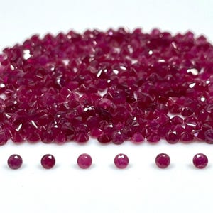 May include: A large collection of small, round, faceted rubies with a deep red colour, arranged in a dense pile with six individual rubies lined up in a horizontal row at the bottom, all displaying a brilliant, reflective, and multi-faceted surface.