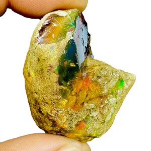 Puede incluir: Una piedra preciosa de ópalo en bruto, sin cortar, con una mezcla de colores. El ópalo muestra destellos de azul, verde, naranja y amarillo dentro de una matriz de color marrón y beige. La piedra tiene una forma natural e irregular, mostrando su belleza en bruto.
