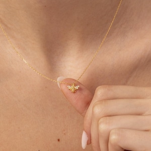 May include: A delicate gold-colored necklace featuring a small bee pendant. The bee pendant has yellow and gold accents. The necklace is shown on a person wearing a light pink top.