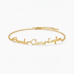 May include: A gold-colored bracelet with the names "Brooke", "Claire", and "Kayla" in cursive script. The bracelet has a delicate chain and a clasp closure. The names are connected and form the centerpiece of the jewelry.