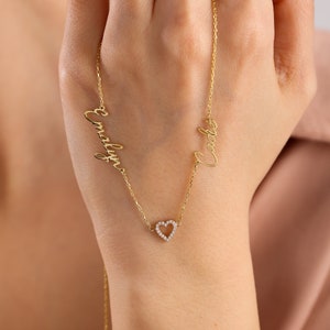 K&ouml;nnte beinhalten: Goldkette mit zwei Namen, "Cody" und "Emily", in Schreibschrift. Die Kette hat einen kleinen Herz-Anh&auml;nger mit einem diamantartigen Glanz.