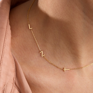 May include: A gold chain necklace with three small letters, L, N, and a cross charm.