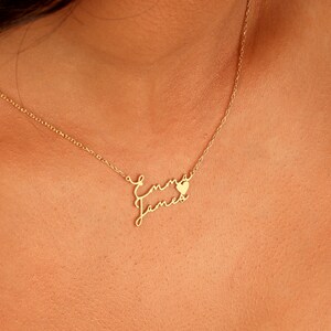 May include: Gold necklace with the names "Emma" and "James" written in cursive script, with a small heart charm between the names.