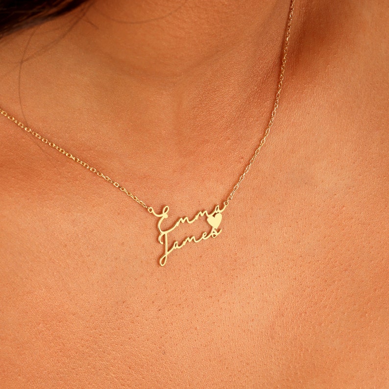 May include: Gold necklace with the names "Emma" and "James" written in cursive script, with a small heart charm between the names.