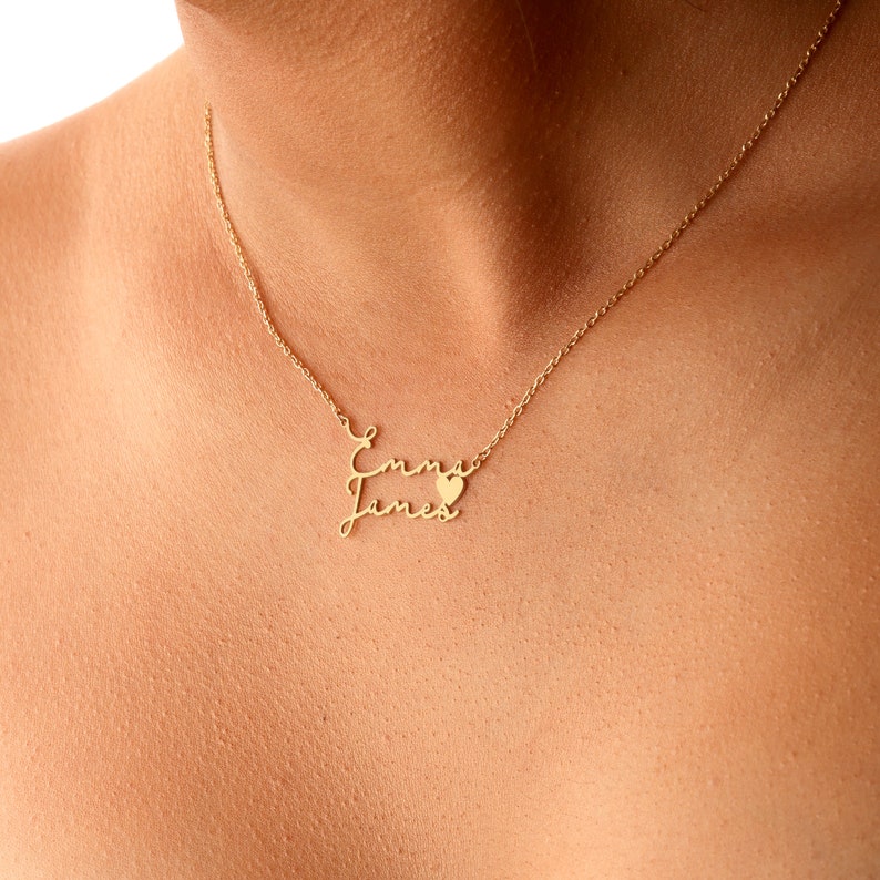 May include: Gold necklace with two names, "Emma" and "James", written in cursive script with a small heart charm between the names.