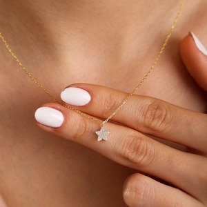 May include: A delicate gold chain necklace with a small, sparkling star pendant. The star is made of tiny diamonds set in gold.