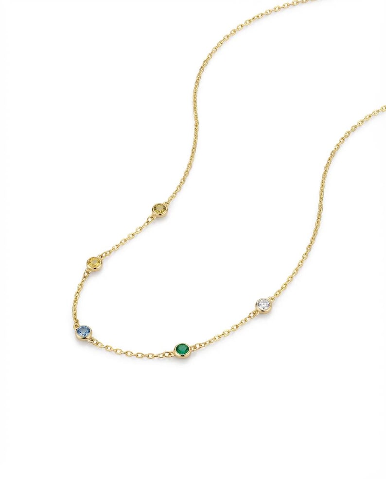 May include: A delicate gold necklace featuring a series of colorful gemstones. The necklace has a fine chain and is adorned with round gemstones in yellow, blue, green, and clear. The gemstones are evenly spaced along the chain, creating a subtle and elegant design.