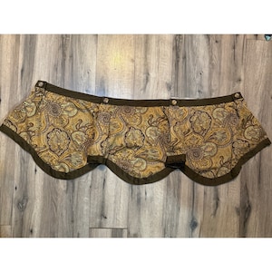 May include: A brown and gold paisley patterned valance with a scalloped edge and brown buttons.