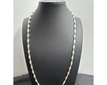 May include: A silver-colored necklace with a twisted rope design. The necklace is displayed on a black mannequin. The chain is made of small, interconnected links that create a textured appearance. The necklace is a simple yet elegant piece of jewelry.