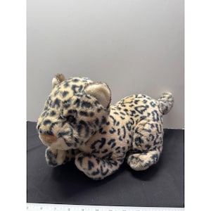 May include: A plush leopard toy in a lying down position. The toy has a tan body with black spots, a white belly, and a brown head with tan ears. The toy is made of soft, fuzzy material.