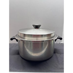 May include: A stainless steel stock pot with a matching lid. The pot features two black side handles and a black knob on the center of the lid. The exterior has a polished metallic finish, and the design includes a wide rim extending outward.