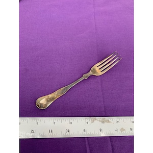 May include: A silver fork with a rounded handle and four tines. The fork is 7 inches long and is lying on a purple surface.
